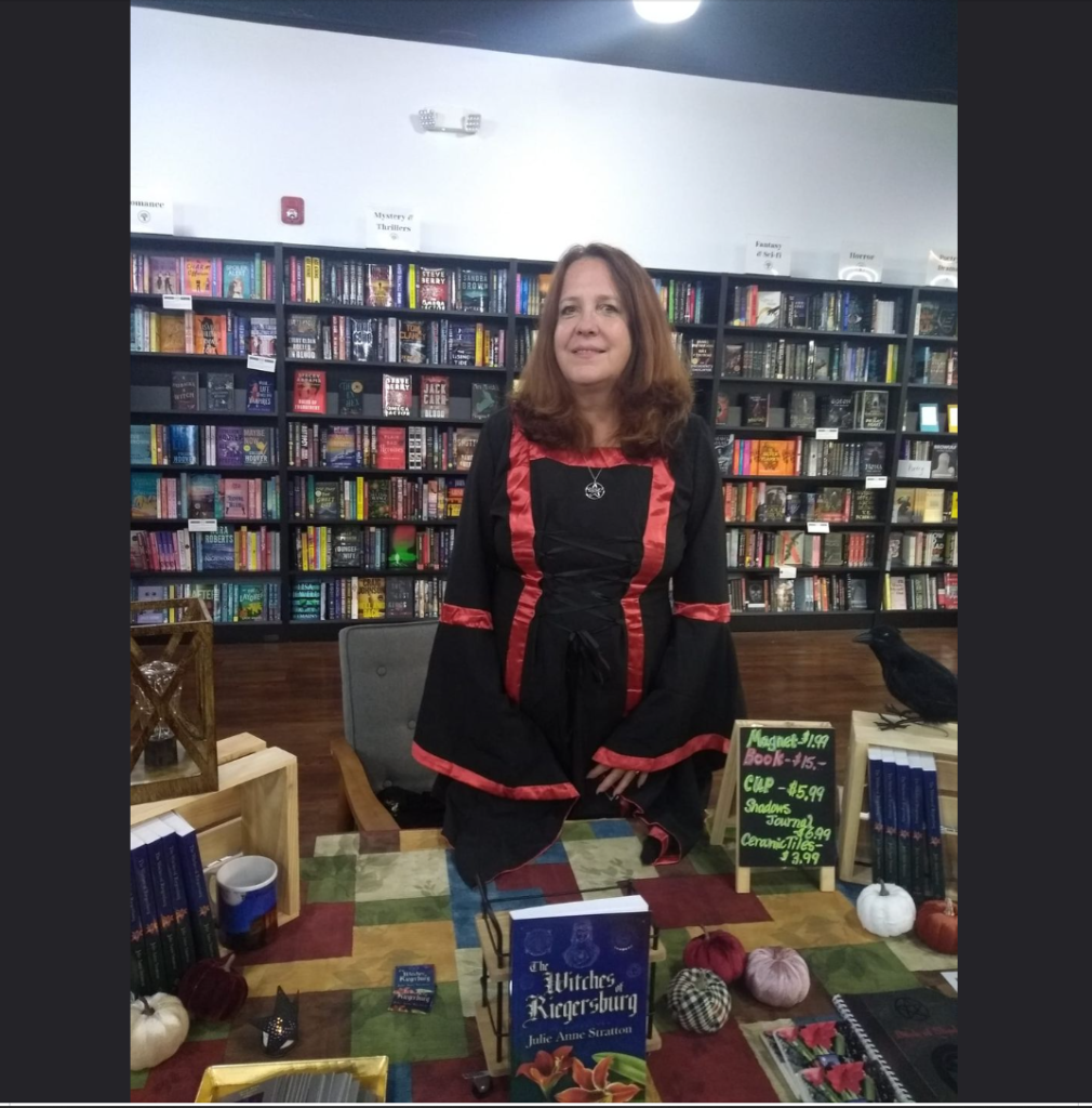 Author Julie Ann Stratton standing in a library, behind a table loaded with books